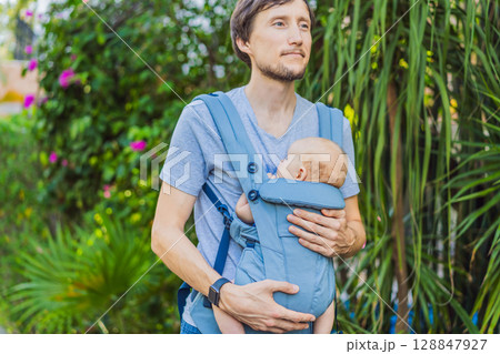 Young father walks in nature with his baby son nestled close in a parent-facing ergonomic baby carrier. Bonding, warmth, and modern parenting concept in a peaceful outdoor setting Young father walks in nature with his baby son nestled close in a parent-facing ergonomic baby carrier. Bonding, warmth, and modern parenting concept in a peaceful outdoor setting 128847927