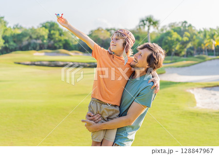 Father and son in the park, the boy wearing a pilot hat and holding a toy airplane, dreaming of adventures. Childhood, bonding, and imagination concept Father and son in the park, the boy wearing a pilot hat and holding a toy airplane, dreaming of adventures. Childhood, bonding, and imagination concept 128847967