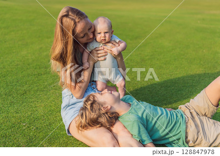 Mother, older son, and newborn baby on a meadow in the park. Family spending quality time together in nature. Parenthood, love, and family bond concept Mother, older son, and newborn baby on a meadow in the park. Family spending quality time together in nature. Parenthood, love, and family bond concept 128847978