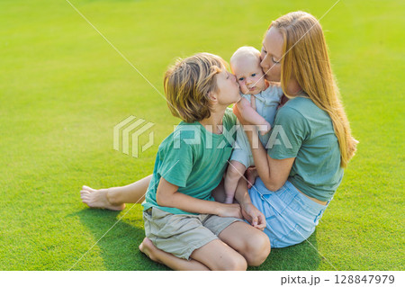 Mother, older son, and newborn baby on a meadow in the park. Family spending quality time together in nature. Parenthood, love, and family bond concept 128847979
