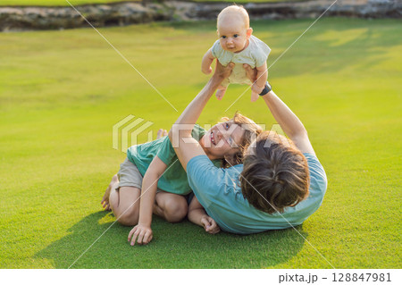 Father, older son, and newborn baby on a meadow in the park. Family spending quality time together in nature. Parenthood, love, and family bond concept Father, older son, and newborn baby on a meadow in the park. Family spending quality time together in nature. Parenthood, love, and family bond concept 128847981