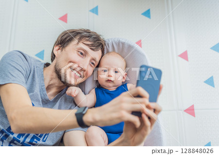 Loving father interacts with his 3-month-old baby lying in a cozy baby nest at home. Tender bonding moment, fatherhood, and early connection in a peaceful family setting 128848026