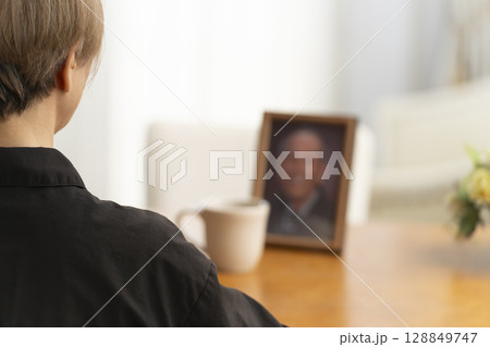 リビングで夫の遺影写真を見ながらティータイムを過ごす女性 リビングで夫の遺影写真を見ながらティータイムを過ごす女性 128849747