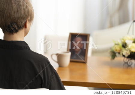 リビングで夫の遺影写真を見ながらティータイムを過ごす女性 リビングで夫の遺影写真を見ながらティータイムを過ごす女性 128849751