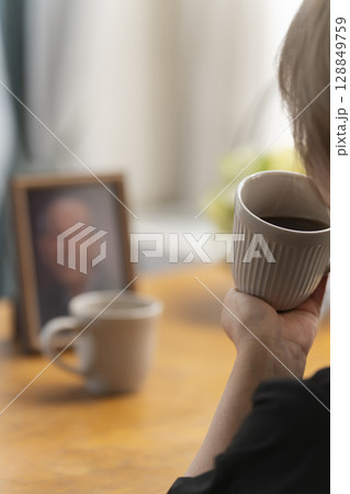 リビングで夫の遺影写真を見ながらティータイムを過ごす女性 128849759