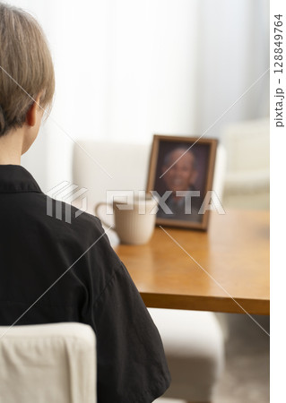 リビングで夫の遺影写真を見ながらティータイムを過ごす女性 128849764