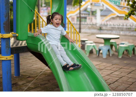 happy toddler baby girl sliding and playing at playground 128850707