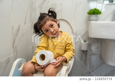 toddler girl sitting on toilet with tissue at home and suffering from stomachache and constipation 128850714