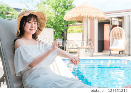 プールサイドのリクライニングチェアに座り日焼け止めクリームを腕に塗る若いアジア人女性 プールサイドのリクライニングチェアに座り日焼け止めクリームを腕に塗る若いアジア人女性 128851213