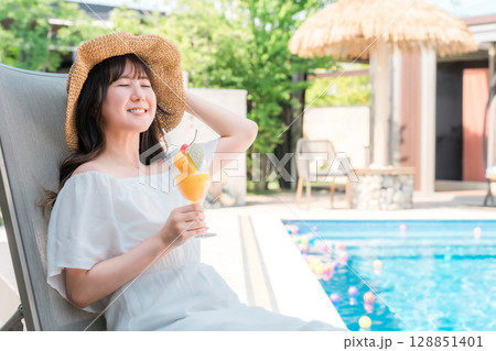 プールサイドのリクライニングチェアに座りトロピカルジュースを飲む若いアジア人女性 128851401