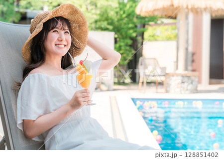 プールサイドのリクライニングチェアに座りトロピカルジュースを飲む若いアジア人女性 128851402