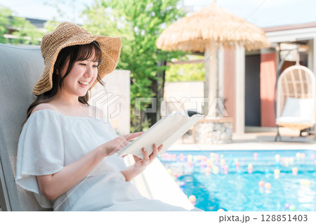 プールサイドでリクライニングチェアに座り読書する若いアジア人女性 プールサイドでリクライニングチェアに座り読書する若いアジア人女性 128851403