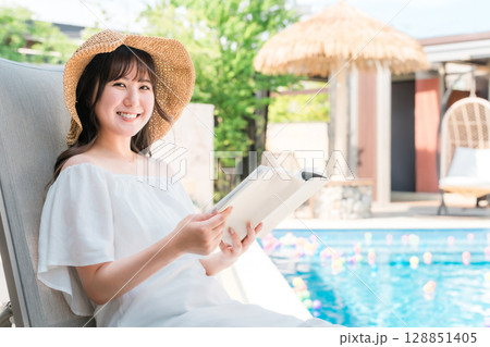 プールサイドでリクライニングチェアに座り読書する若いアジア人女性 プールサイドでリクライニングチェアに座り読書する若いアジア人女性 128851405