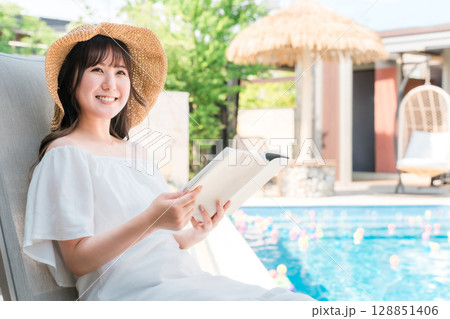 プールサイドでリクライニングチェアに座り読書する若いアジア人女性 プールサイドでリクライニングチェアに座り読書する若いアジア人女性 128851406