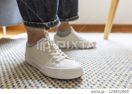 Mens legs in white casual shoes stand on carpet. Mens legs in white casual shoes stand on carpet. 128852669