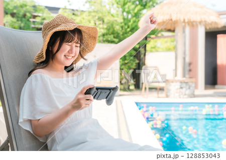 プールサイドでリクライニングチェアに座りゲームをする若いアジア人女性 128853043