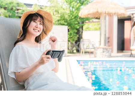 プールサイドでリクライニングチェアに座りゲームをする若いアジア人女性 プールサイドでリクライニングチェアに座りゲームをする若いアジア人女性 128853044