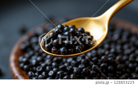 Golden spoon scooping black caviar with wooden bowl full of shiny pearls, showcasing luxury and elegance in food presentation 128853225