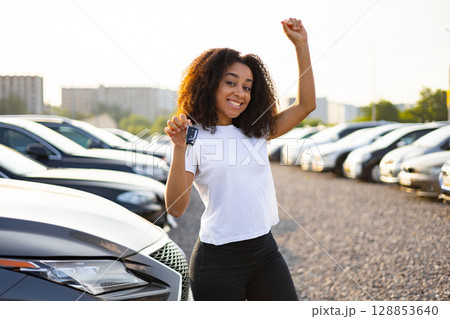 A happy woman celebrates her new car purchase, holding up the keys with excitement in a dealership. A happy woman celebrates her new car purchase, holding up the keys with excitement in a dealership. 128853640