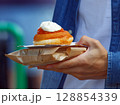 Hand Holding a Delicious Donut Topped With Jam and Cream Outdoors 128854339