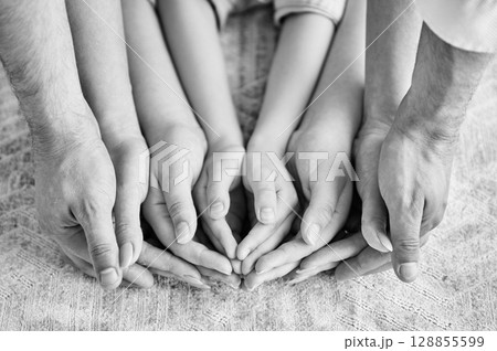 Top view of parents and kids holding empty hands together. Supportive family holding each others hands on background of white carpet. Concepts of teamwork, unity. Black and white image. Top view of parents and kids holding empty hands together. Supportive family holding each others hands on background of white carpet. Concepts of teamwork, unity. Black and white image. 128855599