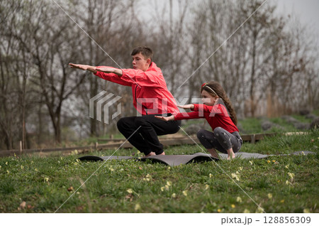 Father and daughter share a joyful moment practicing yoga together in a peaceful outdoor setting surrounded by nature in early spring 128856309