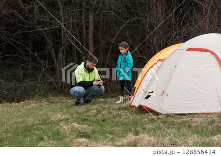 Father and daughter share a moment of joy while camping in nature, exploring the beauty of the outdoors and strengthening their bond in the tranquility of the wilderness Father and daughter share a moment of joy while camping in nature, exploring the beauty of the outdoors and strengthening their bond in the tranquility of the wilderness 128856414