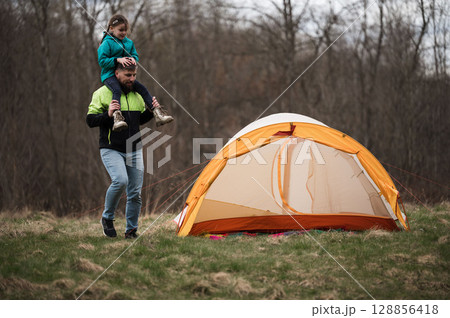 Father and daughter share an adventurous moment during a camping trip in a serene forest at dusk, enjoying nature and each other's company while exploring Father and daughter share an adventurous moment during a camping trip in a serene forest at dusk, enjoying nature and each other's company while exploring 128856418