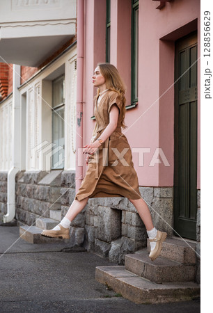 Young woman in linen dress jumping off urban stone stairs in city street 128856629