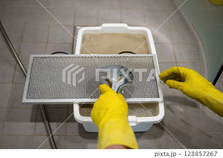 Person rinsing metal kitchen range hood filter with water in sink with yellow rubber gloves Person rinsing metal kitchen range hood filter with water in sink with yellow rubber gloves 128857267