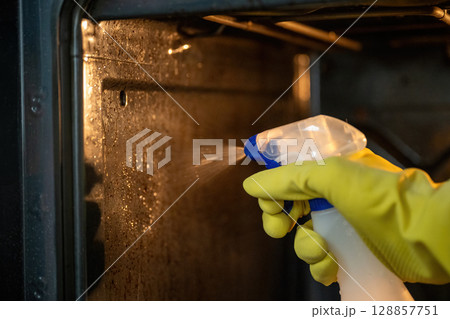 Person spraying degreaser inside dirty oven with yellow rubber gloves 128857751