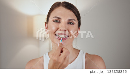 White female teenager with braces demonstrating dental care by using an oral irrigator. She smiles while holding irrigator near her braces, highlighting effective orthodontic hygiene practices. White female teenager with braces demonstrating dental care by using an oral irrigator. She smiles while holding irrigator near her braces, highlighting effective orthodontic hygiene practices. 128858256