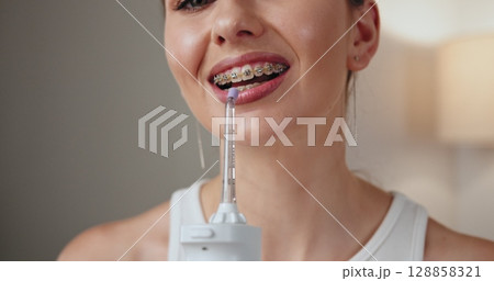 Young Caucasian woman with braces using dental irrigator, emphasizing oral hygiene, dental care, and smile enhancement. 128858321