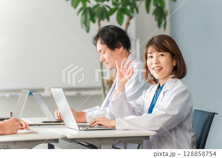 デスクに座り仕事する白衣姿の男女の医師,ドクター 128858754