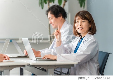 デスクに座り仕事する白衣姿の男女の医師,ドクター 128858758