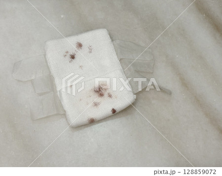 A used gauze pad with dried blood stain, placed on a table top.  128859072