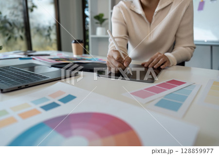 Creative Graphic Designer Working on Digital Tablet with Color Swatches and Laptop in Modern Office Environment 128859977