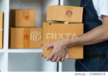 Person Carrying Cardboard Boxes in Warehouse Setting with Shelves in Background for Shipping or Moving Concept Person Carrying Cardboard Boxes in Warehouse Setting with Shelves in Background for Shipping or Moving Concept 128860019