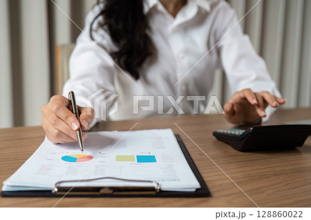 Businesswoman Analyzing Financial Data with Charts and Calculator in Modern Office Setting for Strategic Planning 128860022