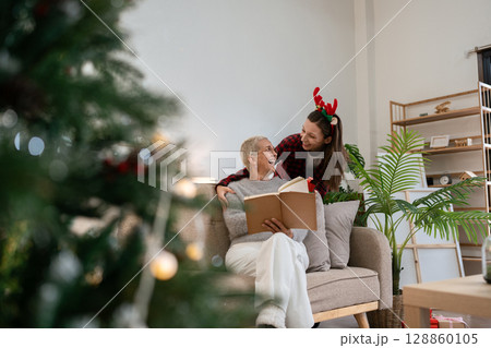 Daughter Surprise gift mother for Christmas while mother was reading book on couch 128860105