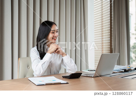 Confident Businesswoman Working on Laptop in Modern Office with Documents and Calculator Confident Businesswoman Working on Laptop in Modern Office with Documents and Calculator 128860117