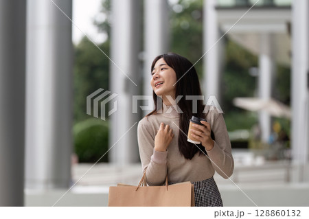 Joyful Woman Shopping on Black Friday with Coffee in Hand, Outdoors in Urban Setting 128860132