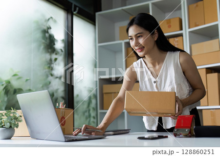 Young Woman Entrepreneur Managing Online Business from Home Office with Laptop and Parcel Boxes 128860251