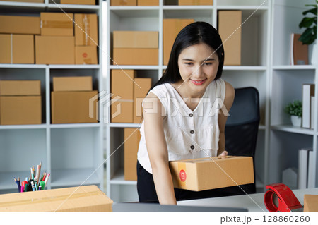 Young Woman Entrepreneur Preparing Packages for Shipping in Modern Home Office with Shelves Full of Boxes Young Woman Entrepreneur Preparing Packages for Shipping in Modern Home Office with Shelves Full of Boxes 128860260