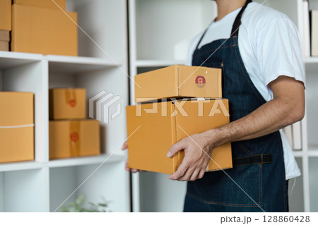 Entrepreneur in Apron Holding Cardboard Boxes in Small Business Warehouse Setting 128860428