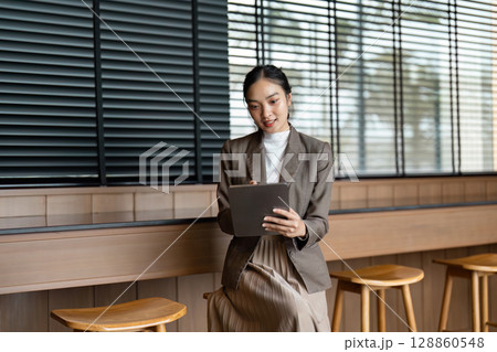 Professional Businesswoman Using Digital Tablet in Modern Office Setting with Natural Light and Wooden Interior Design Professional Businesswoman Using Digital Tablet in Modern Office Setting with Natural Light and Wooden Interior Design 128860548