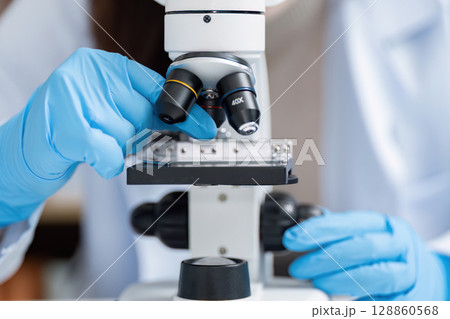 Scientist Using Microscope in Modern Laboratory with Blue Gloves for Scientific Research and Experimentation 128860568