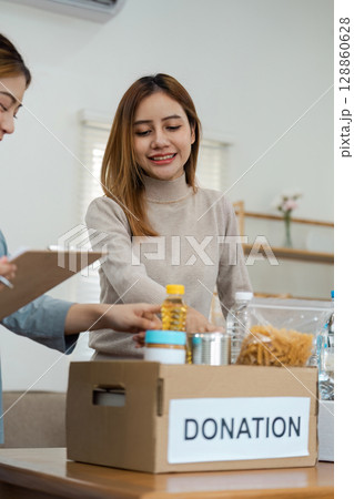 Woman Volunteering at Donation Center Sorting Food Items into Boxes for Charity and Community Support 128860628