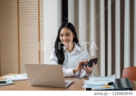 Professional Businesswoman Working on Laptop with Calculator in Modern Office Setting Professional Businesswoman Working on Laptop with Calculator in Modern Office Setting 128860644