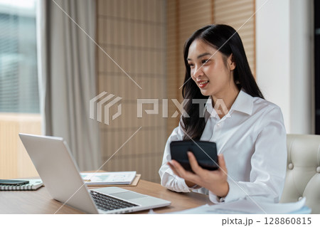 Professional Woman Working from Home Office with Laptop and Smartphone, Smiling and Engaged in Business Tasks Professional Woman Working from Home Office with Laptop and Smartphone, Smiling and Engaged in Business Tasks 128860815